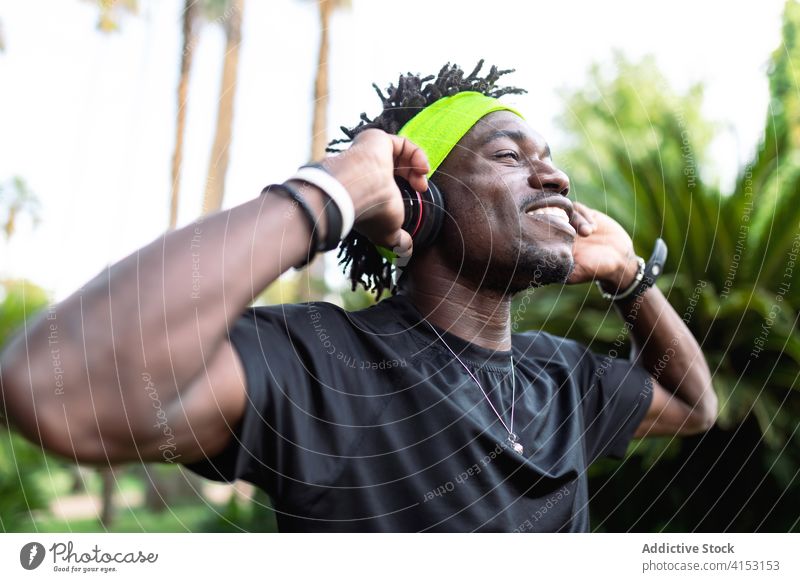 Contemplative ethnic sportsman listening to music with his headphones gesture athlete sporty serene park training style young african american black male