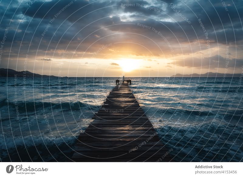 Anonymous person standing on wooden pier in sea at sunset seascape stormy water quay cloudy dramatic playa de alcudia mallorca spain sky sundown shore weather