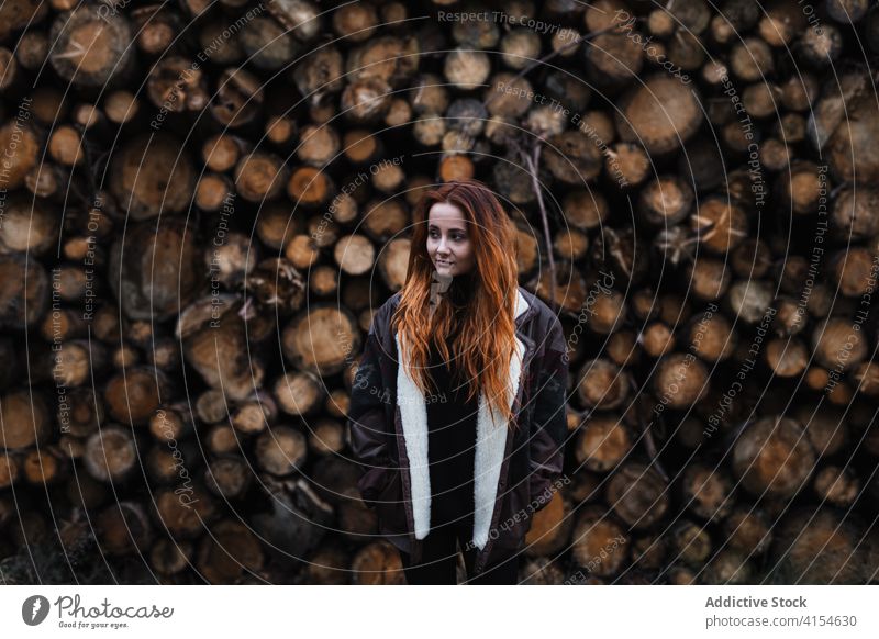 Woman in warm clothes standing near stacked wooden logs woman autumn season woodpile jacket travel young female countryside woodland germany austria resource