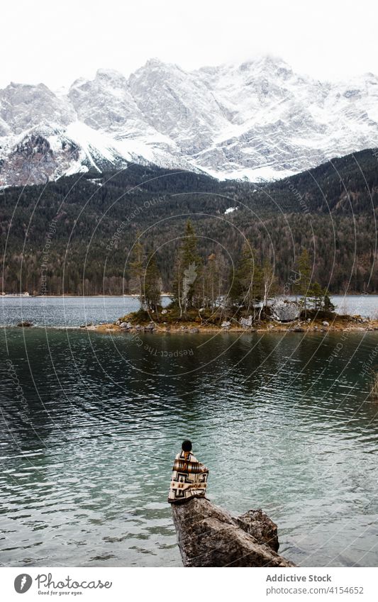 Traveler on rock near lake in winter mountain traveler observe relax shore tourist highland germany austria snow pond stone sit trip water vacation scenic