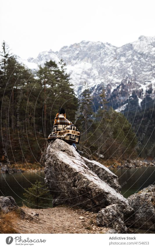 Traveler on rock near lake in winter mountain traveler observe relax shore tourist highland germany austria snow pond stone sit trip water vacation scenic