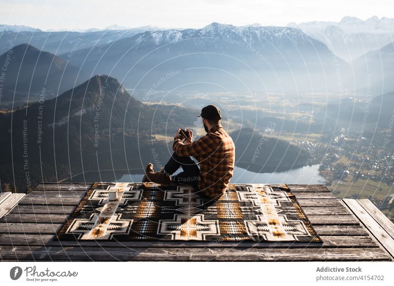 Traveling man sitting on hill and admiring view of mountains photographer photo camera viewpoint taking traveler tourist landscape scenery ridge relax germany