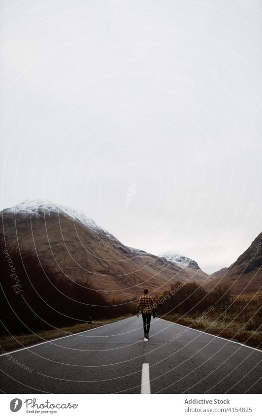 Unrecognizable man on road in mountains travel empty cloudy gloomy highland roadway traveler male scottish highlands scotland uk united kingdom wet journey