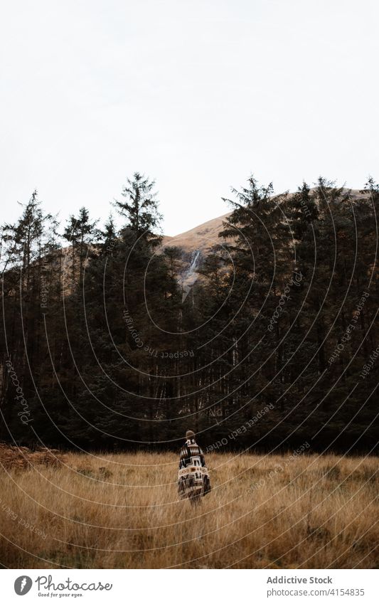 Unrecognizable traveler walking along dry field in highland area explorer mountain vacation gloomy season autumn scottish highlands scotland uk united kingdom