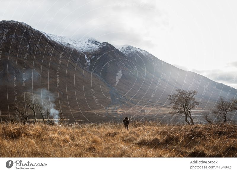 Lonely traveler on meadow near lake in mountainous terrain field admire autumn cold season dry landscape scottish highlands scotland uk united kingdom