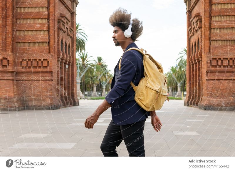 Black man with afro hair and a casual suit walking down the street melody relaxed listening vivid ethnic sound gadget enjoying positive trendy tune stylish