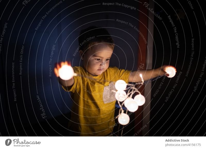 Cute boy playing with garland at home child illuminate glow festive little curious dark apartment room kid joy childhood innocent cute adorable light holiday