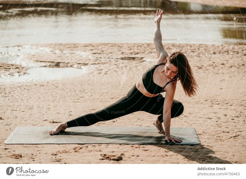 Peaceful woman doing yoga in Skandasana on river bank side lunge skandasana pose outstretch calm zen posture beach female mat balance summer healthy wellness