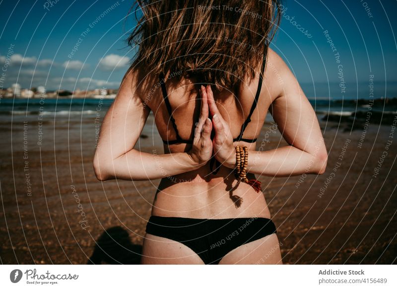 Slim woman doing yoga on seashore namaste gesture hand behind back practice asana pose flexible female sunny seaside nature balance harmony wellness healthy