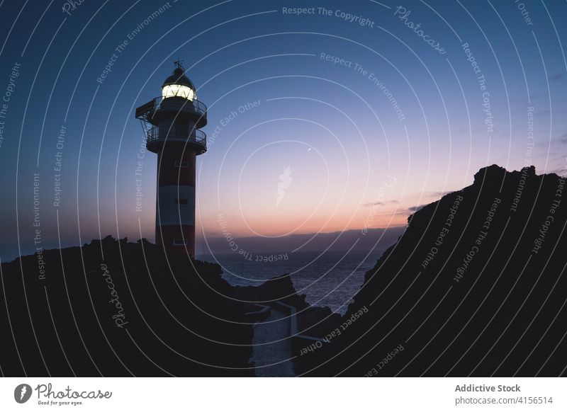 Lighthouse on cliff in evening lighthouse illuminate sea navigate guide beacon sunset spectacular tenerife sky canary island spain rocky hill breathtaking