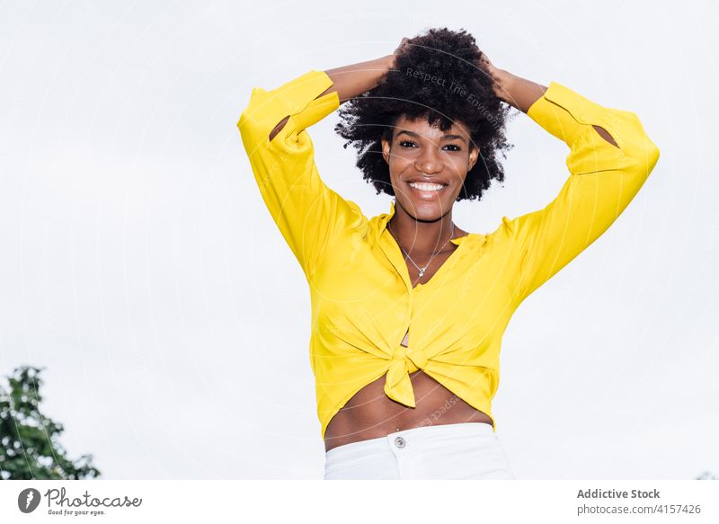 Optimistic black woman in trendy clothes smiling for camera and dancing with raised arms on sunny day in park dance smile style summer arm raised daytime fun