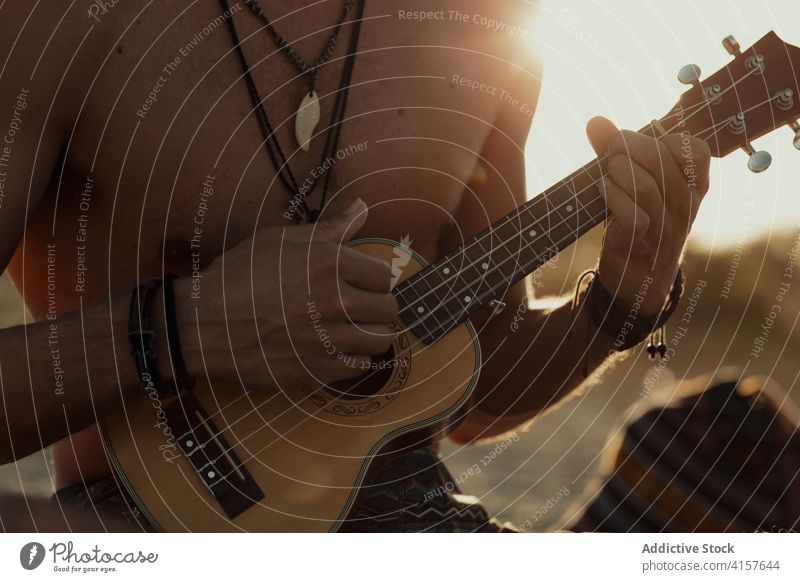 Creative man playing ukulele on beach hippie entertain acoustic music creative male sunset summer shore rest vacation weekend guitar joy sit enjoy relax