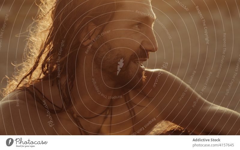 Calm man relaxing on beach at sundown sunset summer enjoy tranquil long hair carefree handsome evening male sand shore sit coast vacation naked torso shirtless