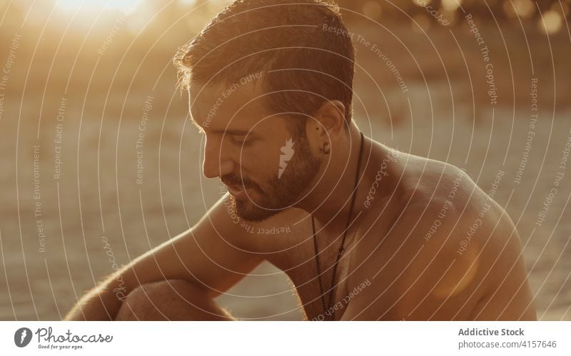 Calm man relaxing on beach at sundown sunset summer enjoy tranquil carefree handsome evening male sand shore sit coast vacation naked torso shirtless serene