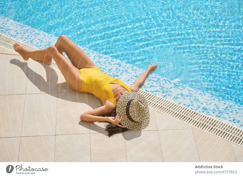 Slim woman in hat sunbathing at poolside summer lying chill enjoy resort relax rest female slim leisure tourist suntan wellness wellbeing travel tourism