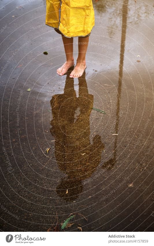 Vertical photo a barefoot person in a raincoat reflected in a puddle poor dramatic skin wet weather drop reflection children climate symmetry legs path image