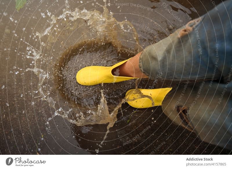 Aerial view of the yellow rain boots hitting a puddle splashing water step joke innocence lifestyles messy aerial playful kids enjoyment wet weather drop