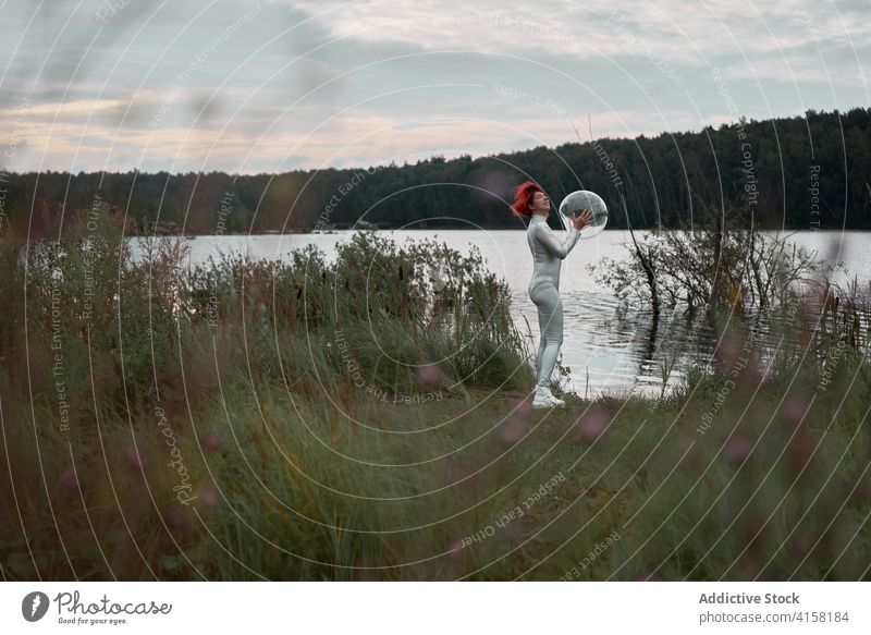 Woman in astronautic suit standing near water woman futuristic space helmet river nature cosmonaut concept female silver future fantasy science explore planet