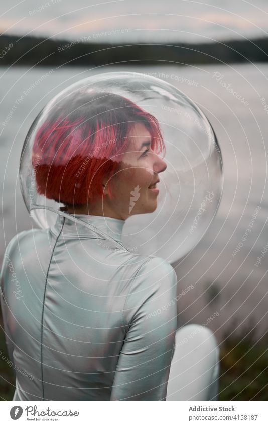 Woman in astronautic suit sitting near water woman futuristic space helmet river nature smile cosmonaut concept female silver future fantasy science explore