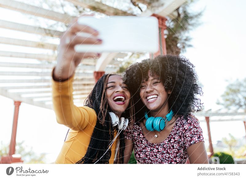 Cheerful black friends taking selfie in city hug smartphone women friendship cheerful bonding using summer promenade ethnic african american braid curly hair