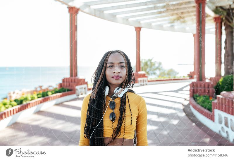 Black woman with headphones on embankment braid appearance charming promenade individuality summer creative calm female ethnic black african american enjoy