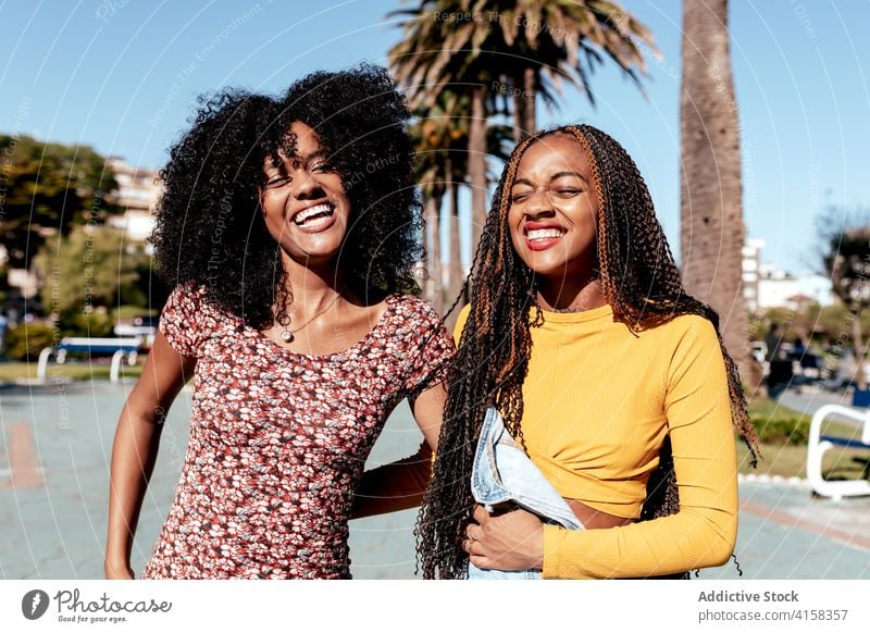 Smiling black women walking along street together friend tropical holding hands delight friendship best friend summer ethnic african american happy town