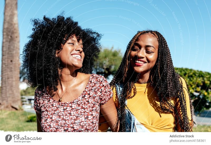 Smiling black women walking along street together friend tropical holding hands delight friendship best friend summer ethnic african american happy town