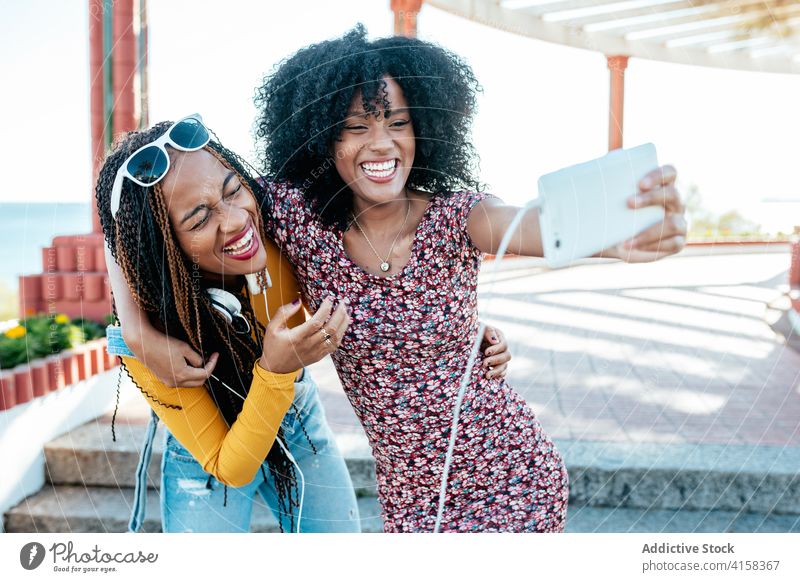 Cheerful black friends taking selfie in city hug smartphone women friendship cheerful bonding using summer promenade ethnic african american braid curly hair