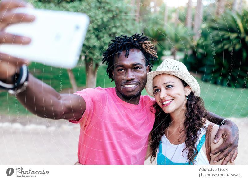 Smiling multiethnic couple taking selfie in park travel smartphone moment enjoy adventure wanderlust using multiracial diverse black african american green