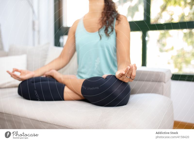 Peaceful woman meditating in Lotus pose at home mindfulness stress relief lotus pose yoga padmasana meditate relax vitality tranquil practice sofa mudra