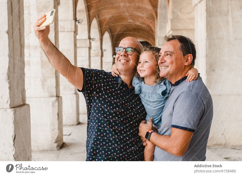 Cheerful LGBT family taking selfie in city lgbt child couple gay men girl smartphone homosexual together take photo self portrait cute daughter street smile