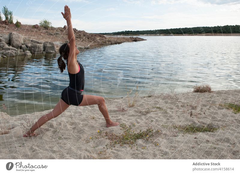 Young woman doing balancing yoga asana near lake practice warrior virabhadrasana pose balance stand harmony wellness lifestyle female concentrate mindfulness