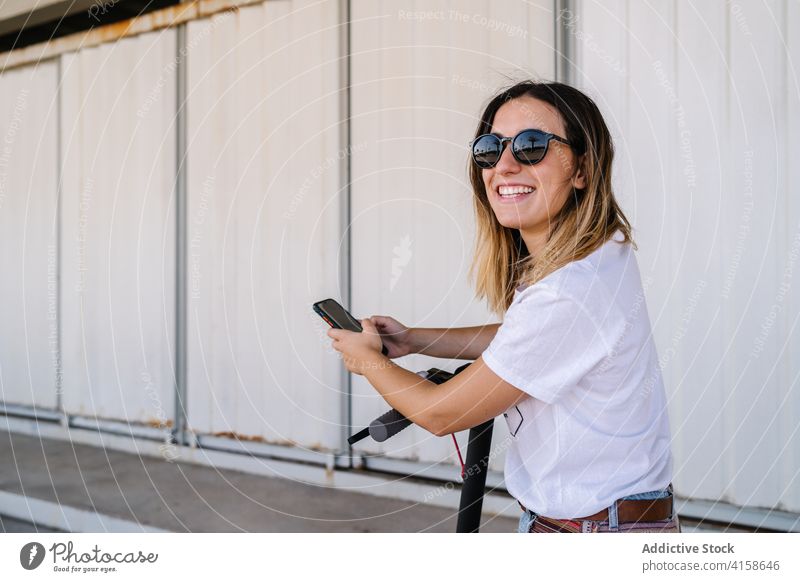 Cheerful woman with electric scooter using smartphone cheerful mobile app transport ride happy urban vehicle alternative eco friendly young female browsing