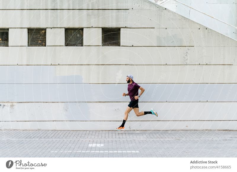 Fit man running along street in city runner urban training cardio fit endurance male dynamic pavement moment sportsman active healthy exercise sportswear