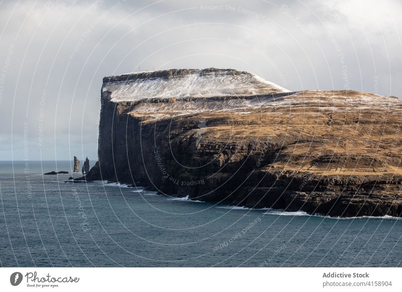 Rocky cliff near sea on Faroe Islands rock seascape winter snow season cold steep terrain faroe islands rocky scenery majestic coast shore water sky calm