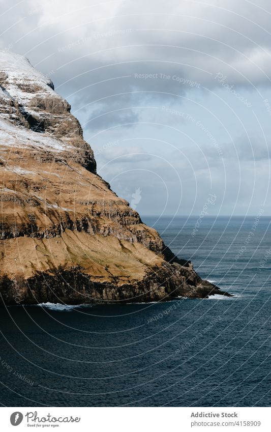 Rocky cliff near sea on Faroe Islands rock seascape winter snow season cold steep terrain faroe islands rocky scenery majestic coast shore water sky calm