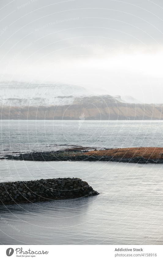 Rocky cliff near sea on Faroe Islands rock seascape winter snow season cold steep terrain faroe islands rocky scenery majestic coast shore water sky calm