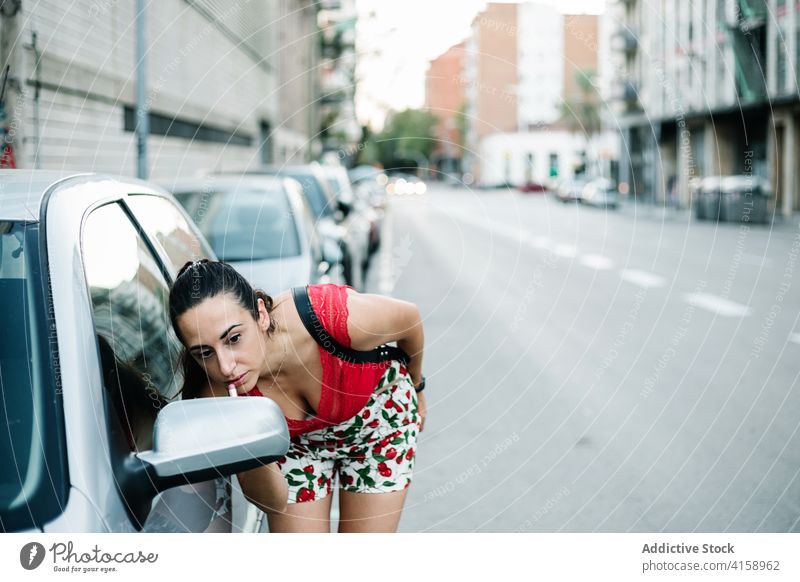 Woman applying lipstick near car mirror woman makeup street urban roadside beauty cosmetic young female brunette glamour style fashion lifestyle city vehicle