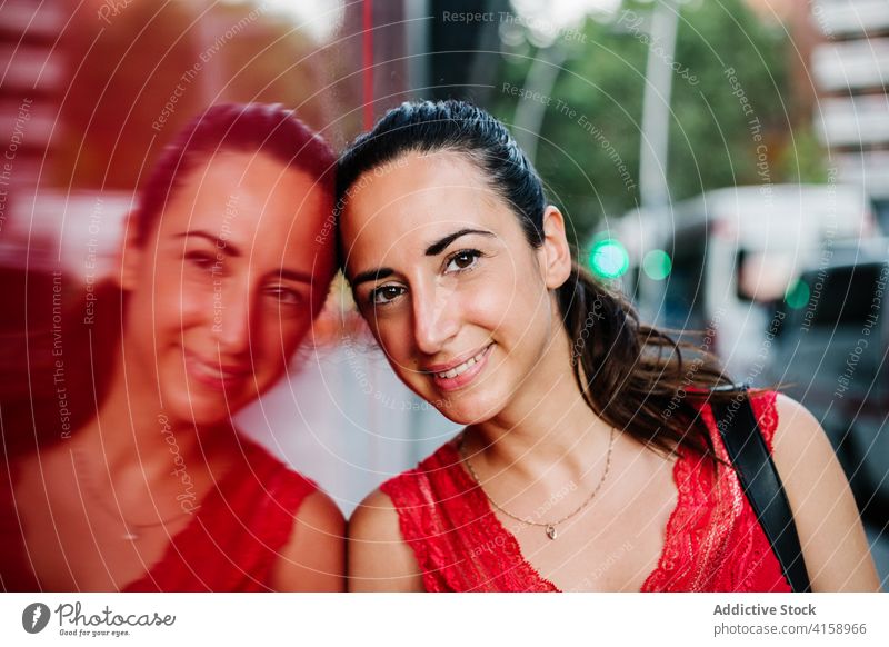 Happy ethnic woman standing on city street smile happy urban glass wall reflection cheerful modern friendly young hispanic female positive contemporary