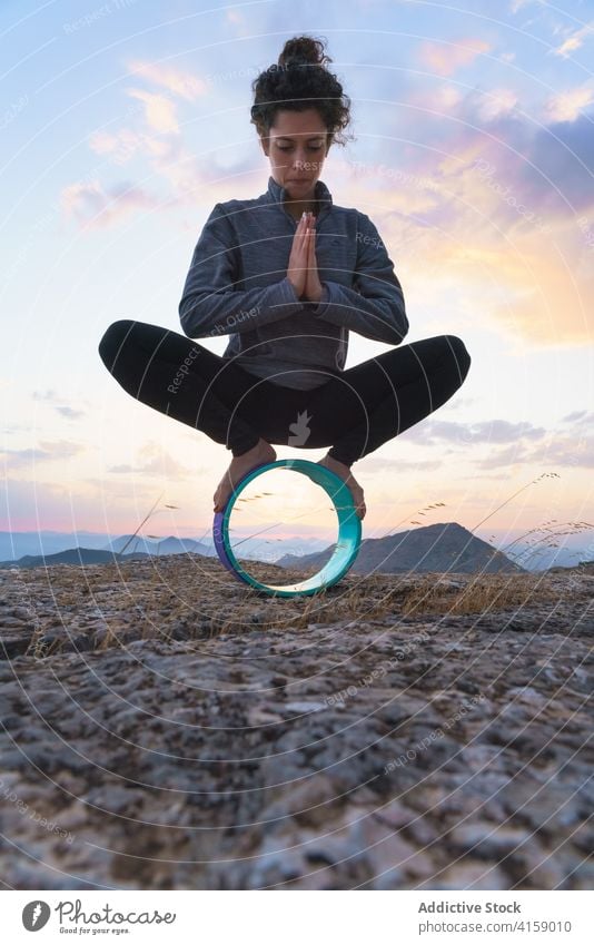 Young woman balancing on yoga wheel in nature balance malasana garland equipment pose mountain rock practice position wellness harmony wellbeing zen health care