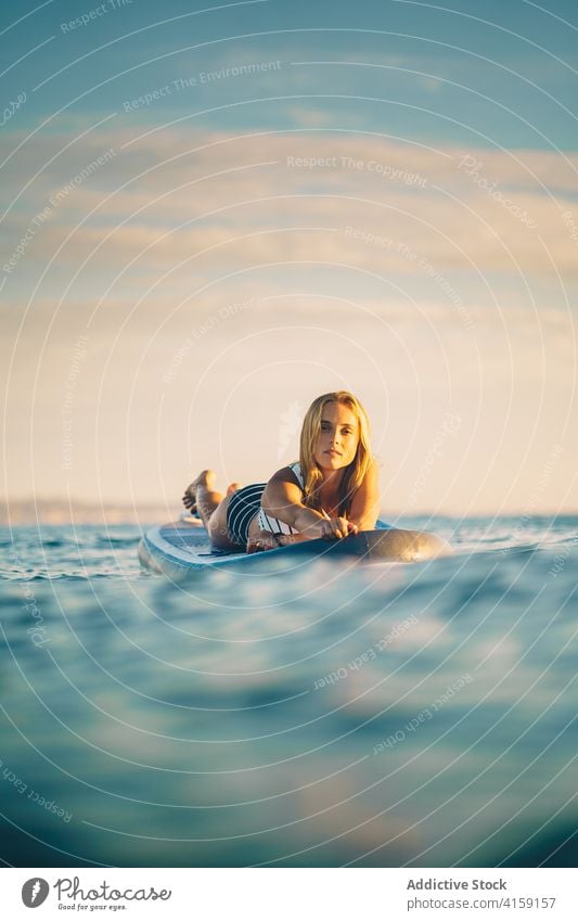 Serene woman on surfboard in sea lying relax sunset slim swimsuit water wave female sky recreation ocean summer swimwear rest weekend peaceful holiday calm