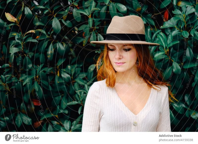 Young woman in hat standing in garden style redhead trendy red hair modern ginger vogue young female fashion long hair lady confident charming lifestyle elegant