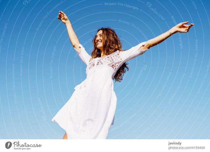 Young woman raising her arms in a beautiful white dress against a blue sky fashion girl wave open hair female copyspace extensions hairstyle fashionable model