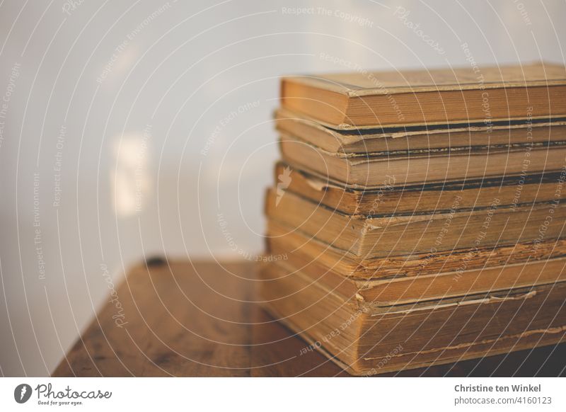 A stack of old, yellowed and torn books lies on a small wooden table in front of a bright wall with sun reflections. World Book Day on 23 April. pile of books