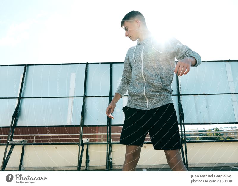 Rider on waveboard plays in abandoned parking lot teenager sweatshirt layered haircut alone rooftop seriousness clear sky shorts sport young leisure game