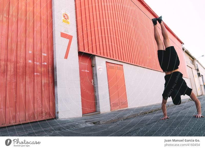 Young man with cap and black clothes does a handstand faced industrial building with the number seven Handstand balance adolescent Acrobatic young local red