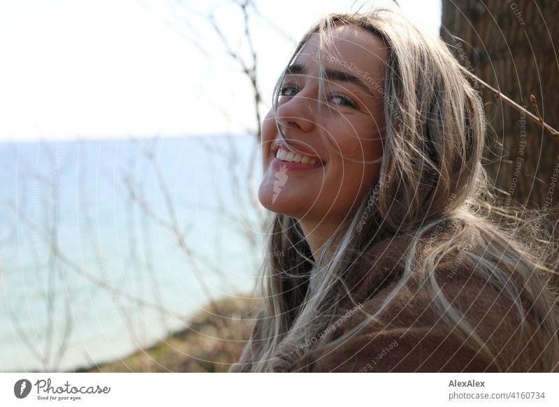 A beautiful blond girl stands on the Baltic Sea beach near the cliff, smiles and looks into the camera Girl Smiling joyfully Landscape by Blonde Joy