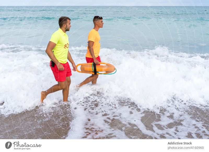 Lifeguards with torpedo rescue buoys strolling on sea beach lifeguard lifesaver ocean friend barefoot horizon nature seascape sandy coast walk uniform fit