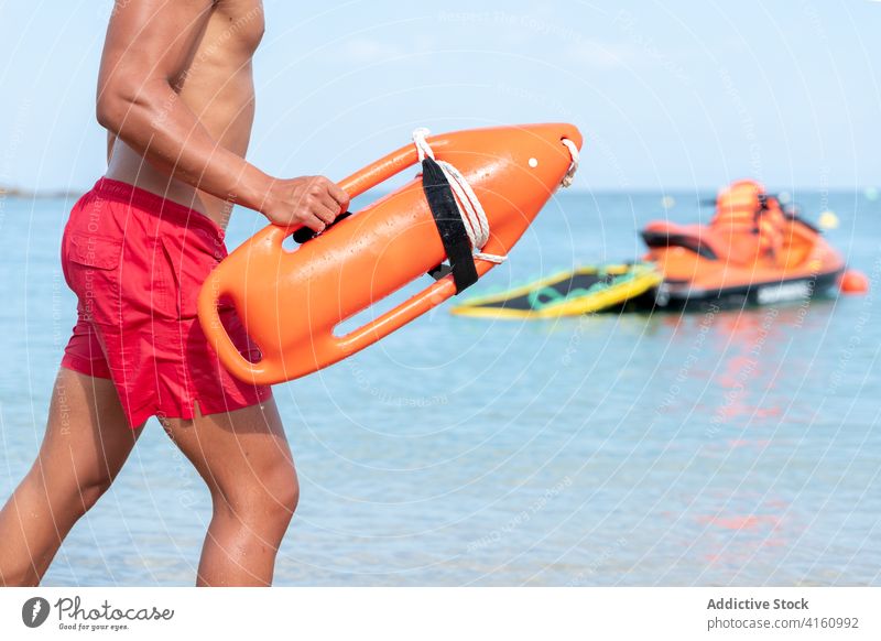 Unrecognizable lifeguard with torpedo life savers on ocean lifesaver walk shore coworker mask covid 19 men barefoot sea ripple water rescue buoy bright