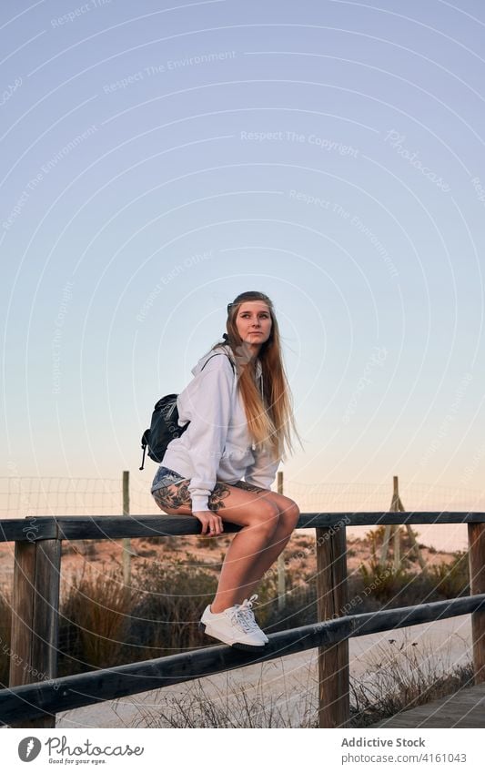 Peaceful woman sitting on fence at sunset travel browsing twilight relax embankment female wooden traveler calm vacation rest connection sundown lady summer bag